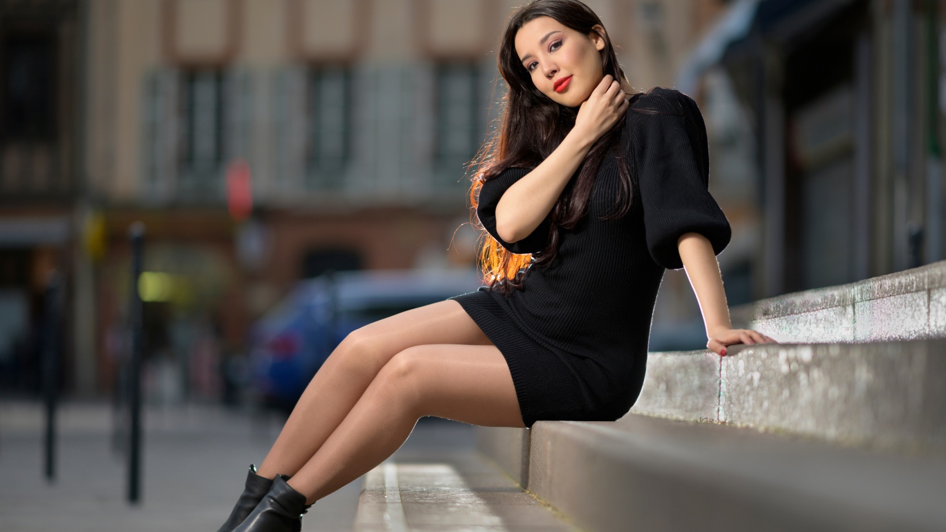 Красивая девушка в черном платье сидит на ступенях