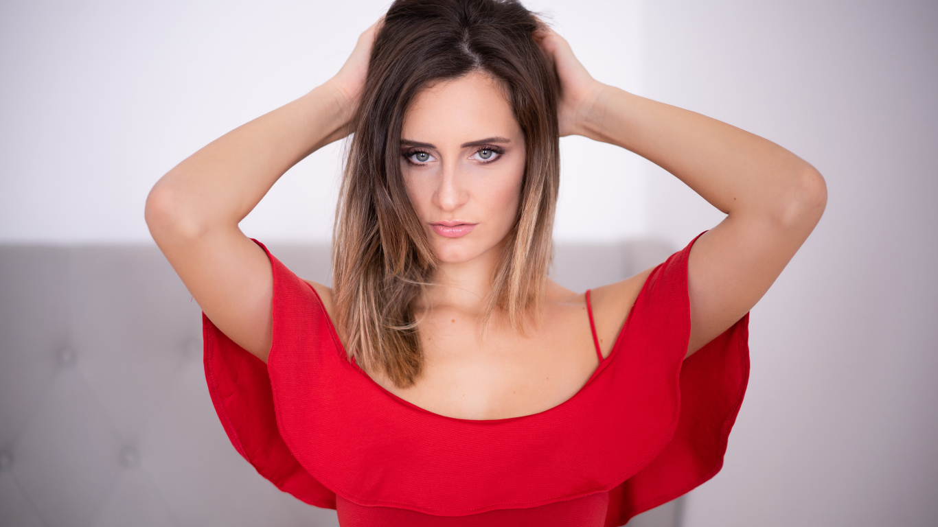 Красивая девушка в красном платье с руками в волосах