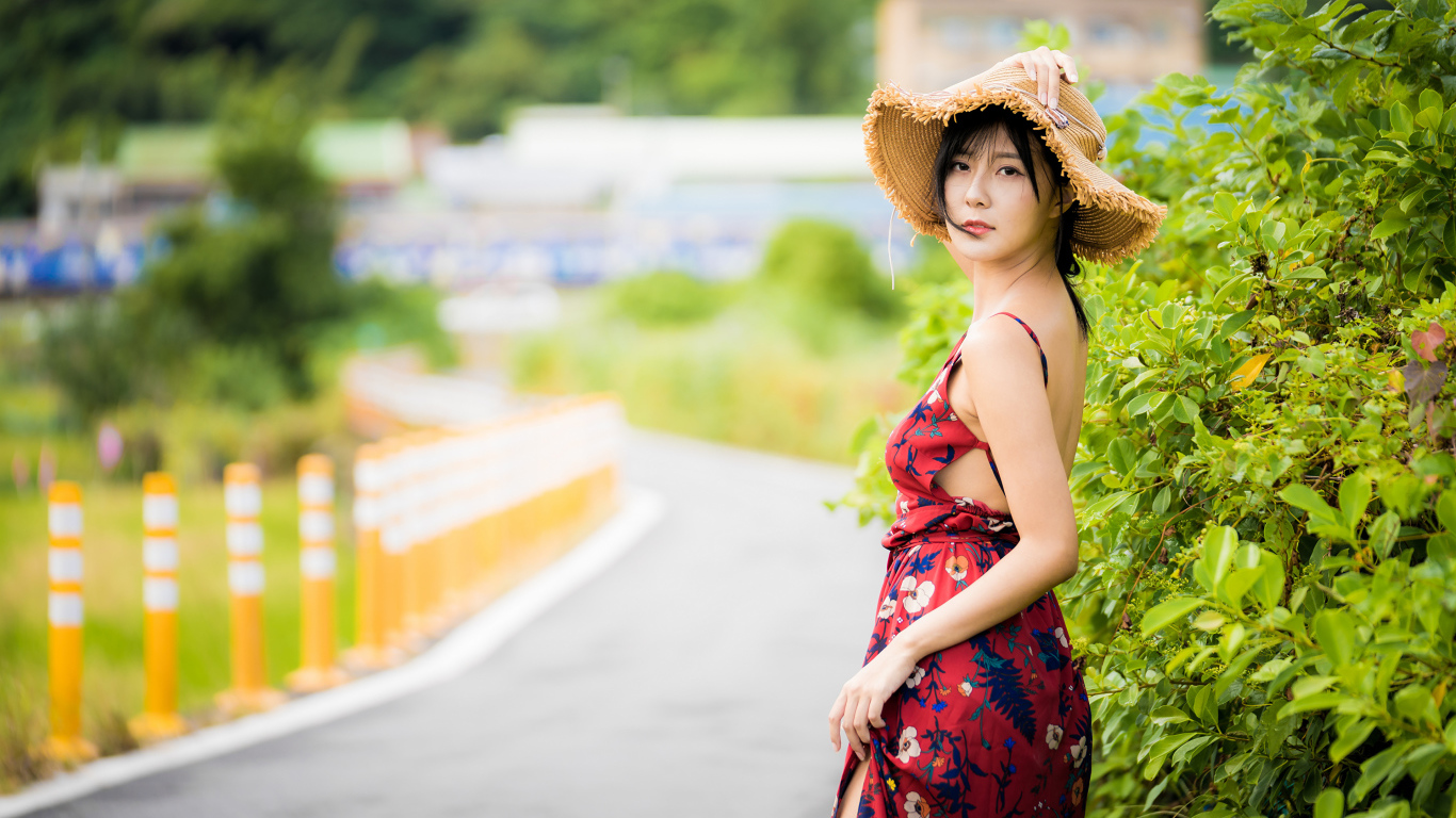 Красивая девушка в сарафане со шляпой на голове у куста 