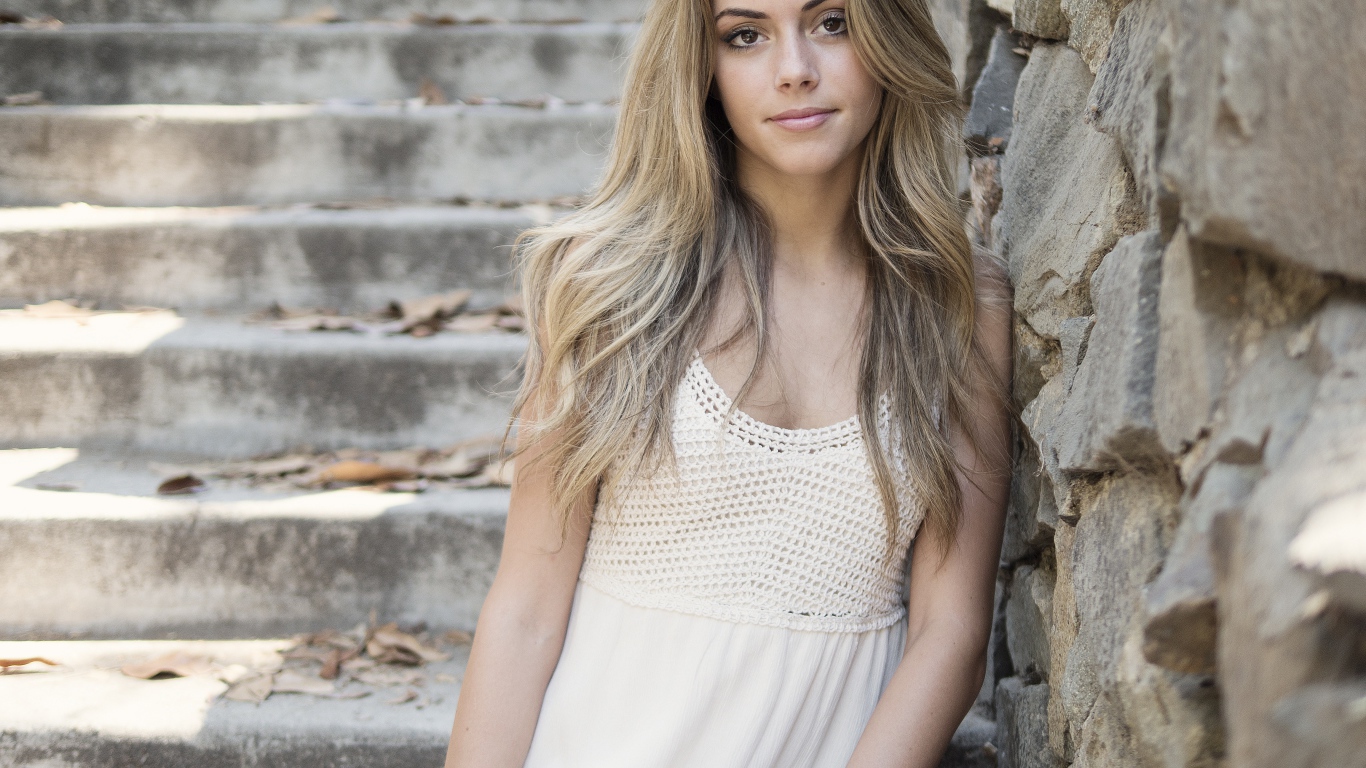 Красивая девушка в белом платье у каменной стены 