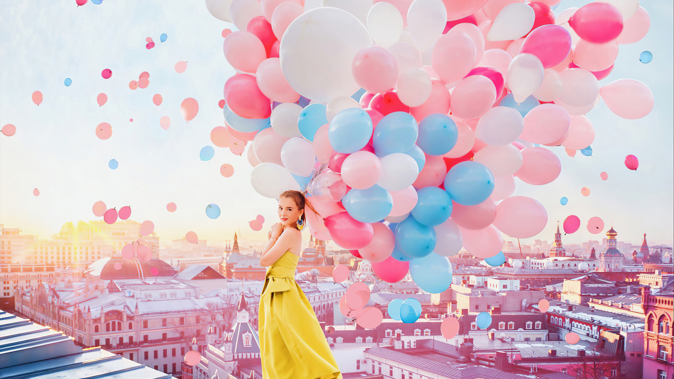 Красивая девушка в желтом платье стоит на крыше с воздушными шариками