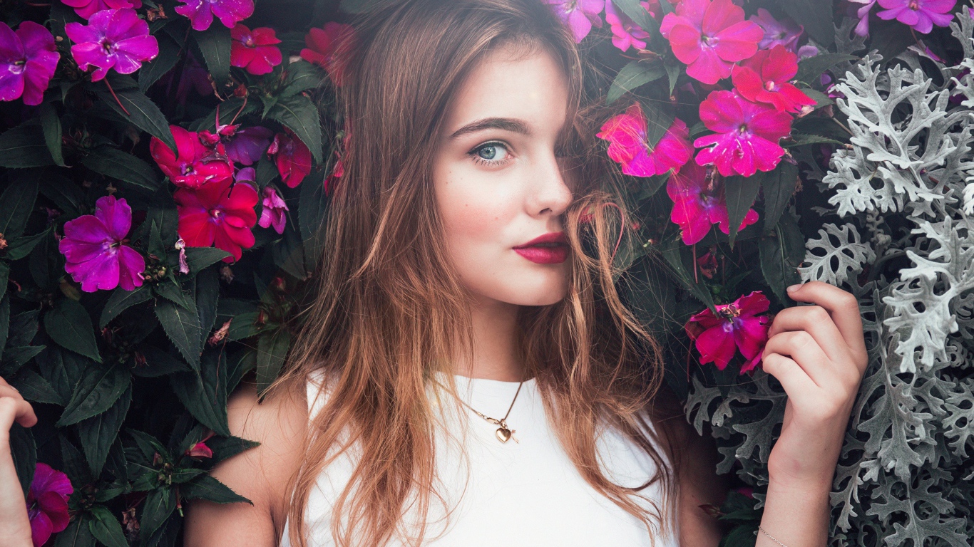 Красивая девушка стоит у зарослей с розовыми цветами