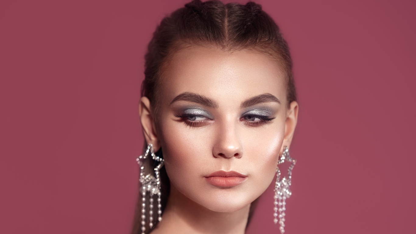 Красивая девушка с макияжем и большими серьгами на розовом фоне