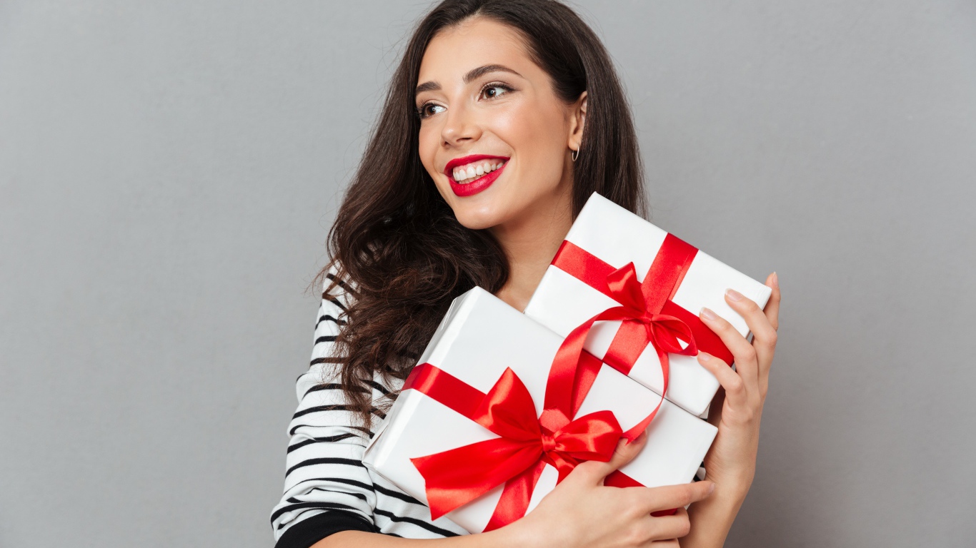 Красивая улыбающаяся девушка с подарками в руках на сером фоне 