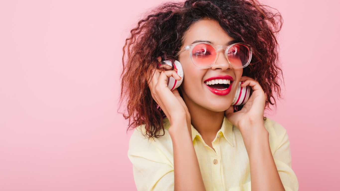 Яркая улыбающаяся девушка слушает музыку в наушниках 