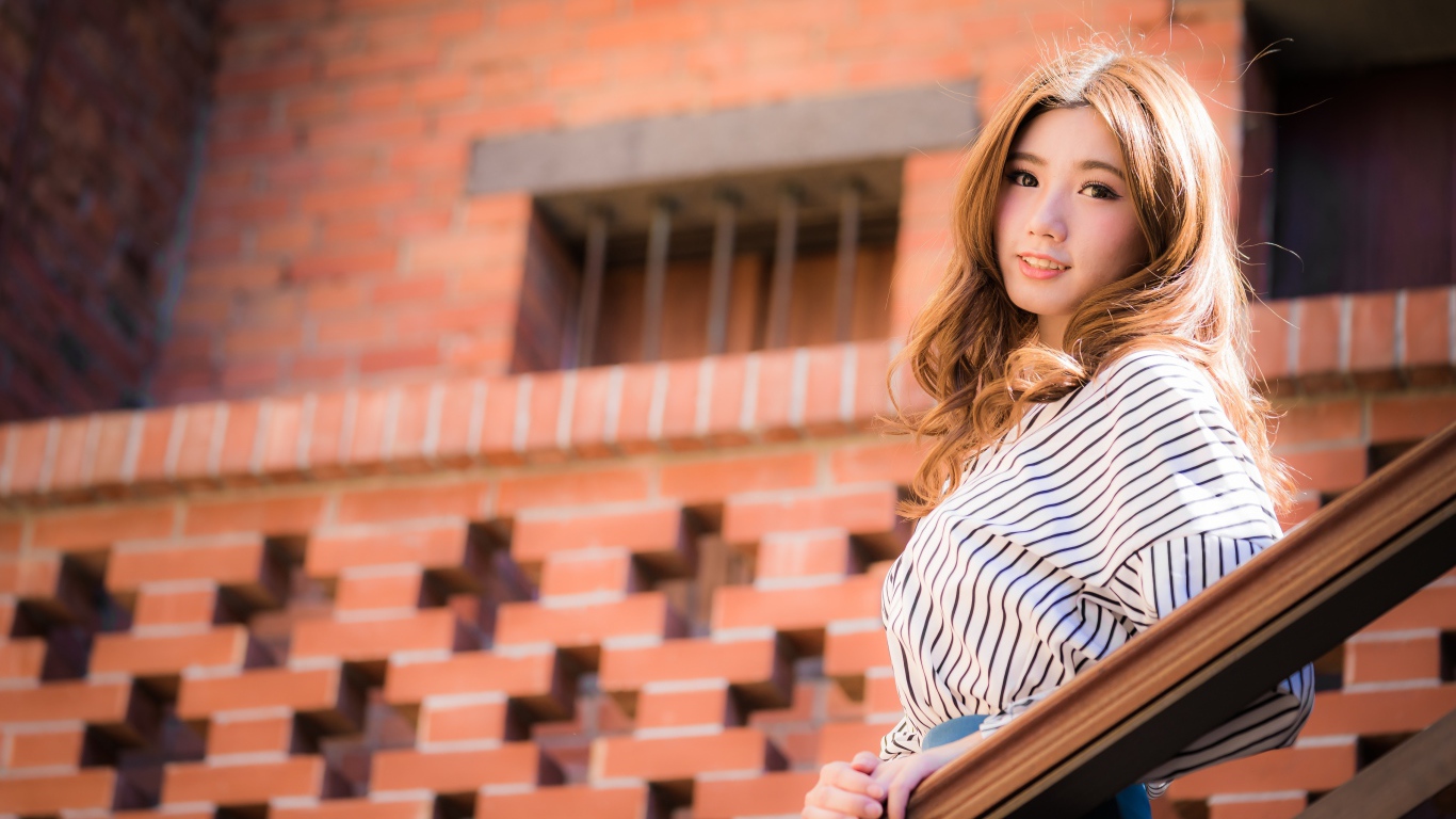 Милая девушка в полосатой рубашке стоит на ступеньках 