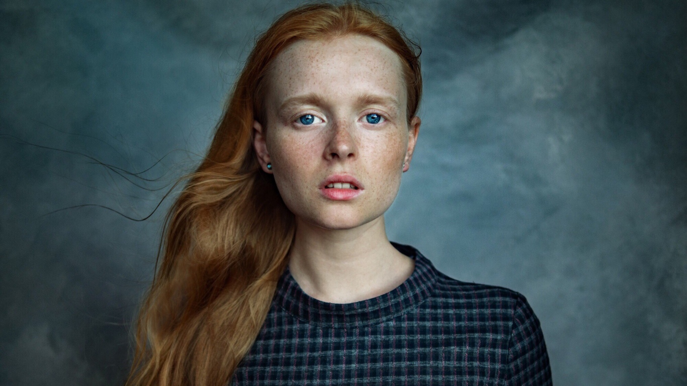 Милая рыжеволосая голубоглазая девушка с веснушками на лице на сером фоне