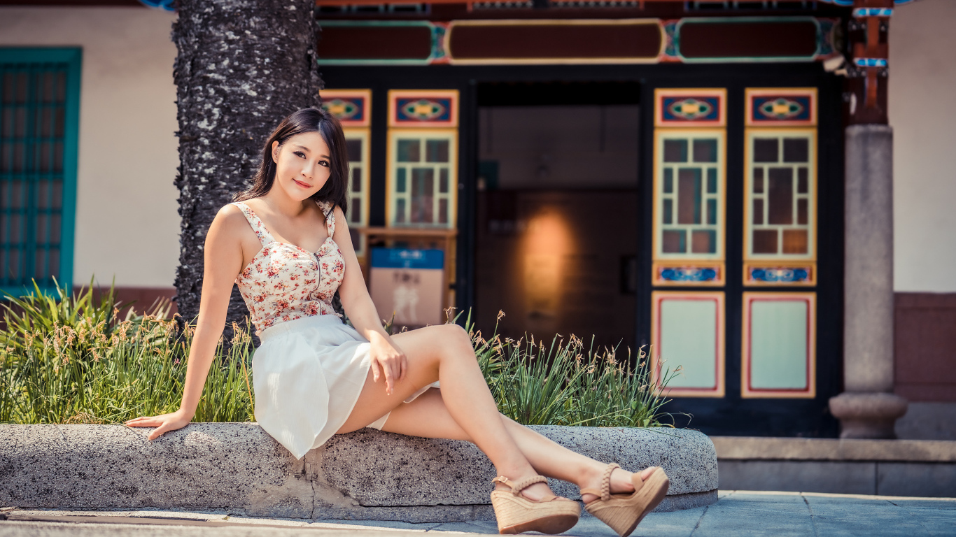 Милая улыбающаяся девушка сидит на бордюре