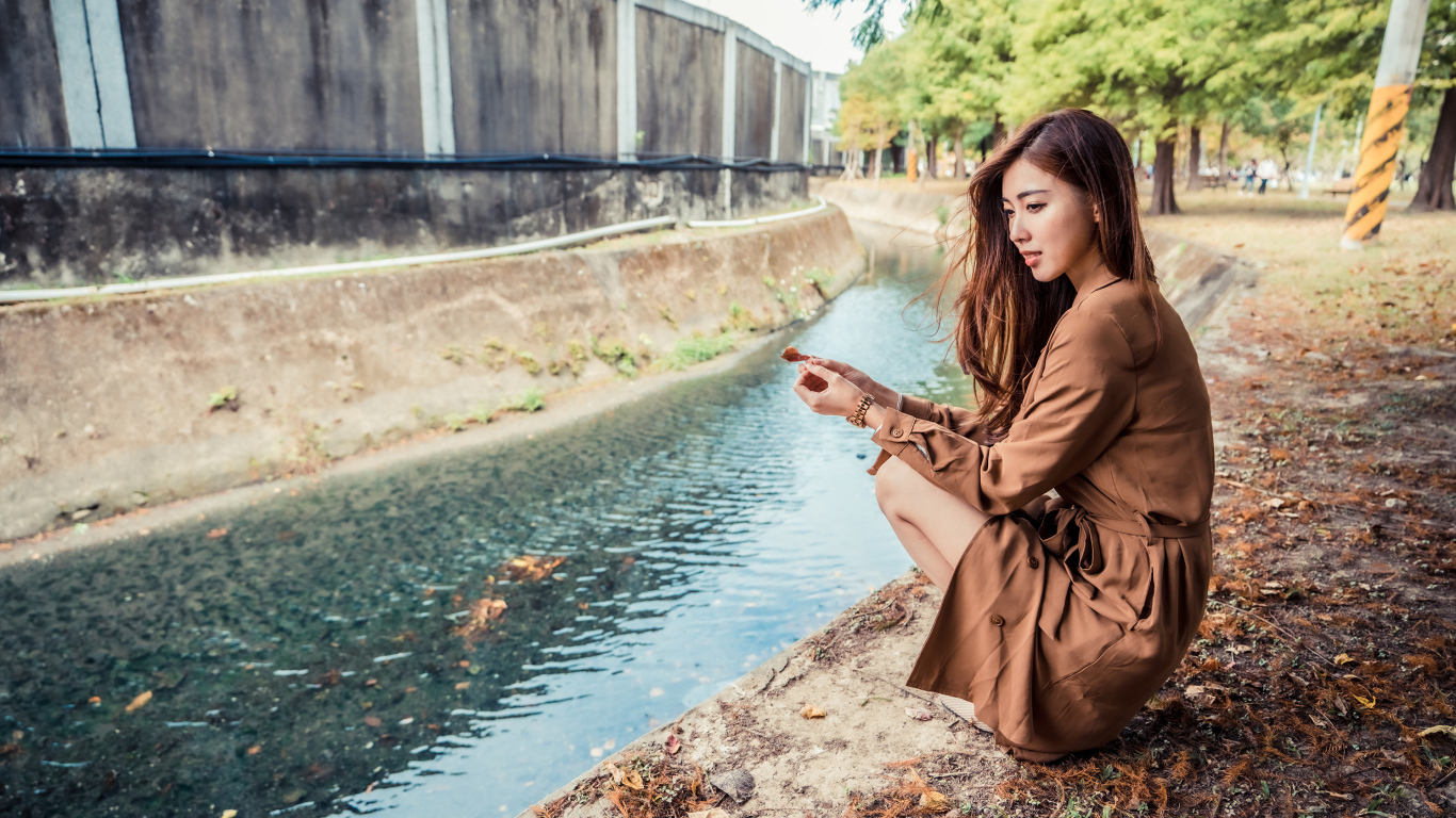 Мечтательная девушка азиатка сидит у воды