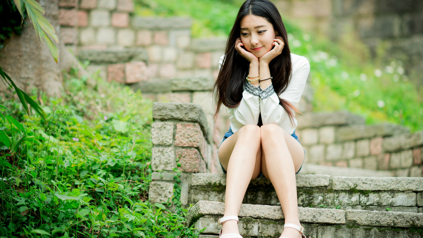 Мечтательная девушка азиатка сидит на ступеньках 