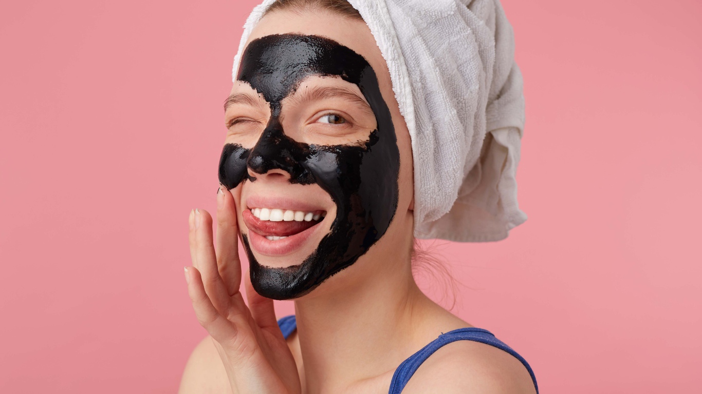 Смешная молодая девушка с черной косметической маской на лице 