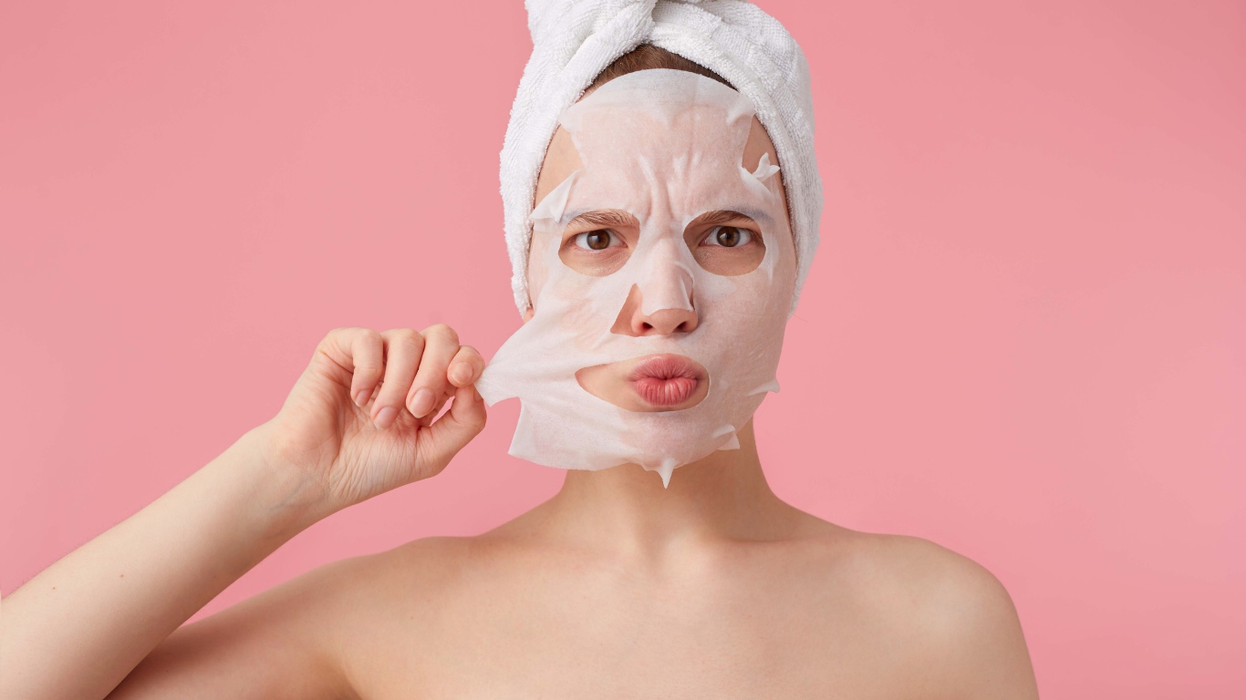 Девушка снимает косметическую маску с лица на розовом фоне 