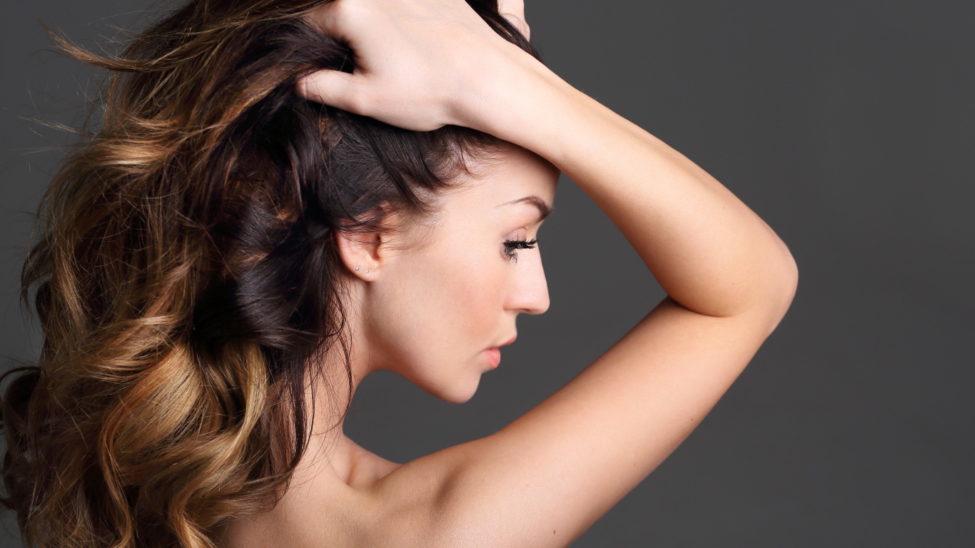 Девушка с руками в волосах на сером фоне