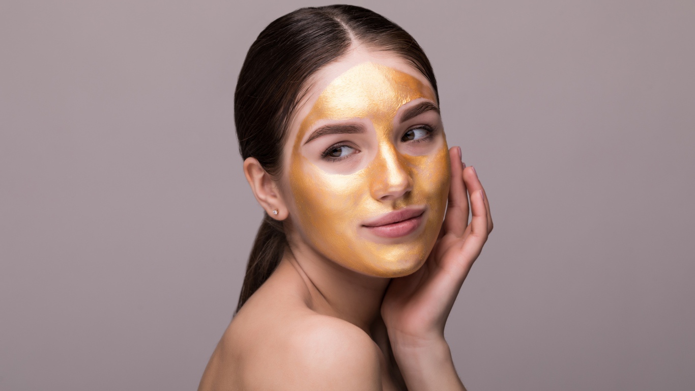 Золотая маска на лице у молодой девушки 