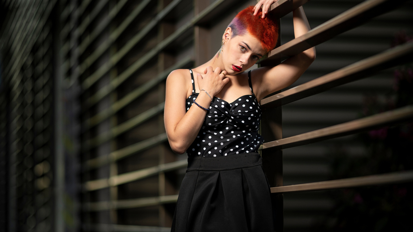 Эпатажная девушка с короткой стрижкой стоит у забора 