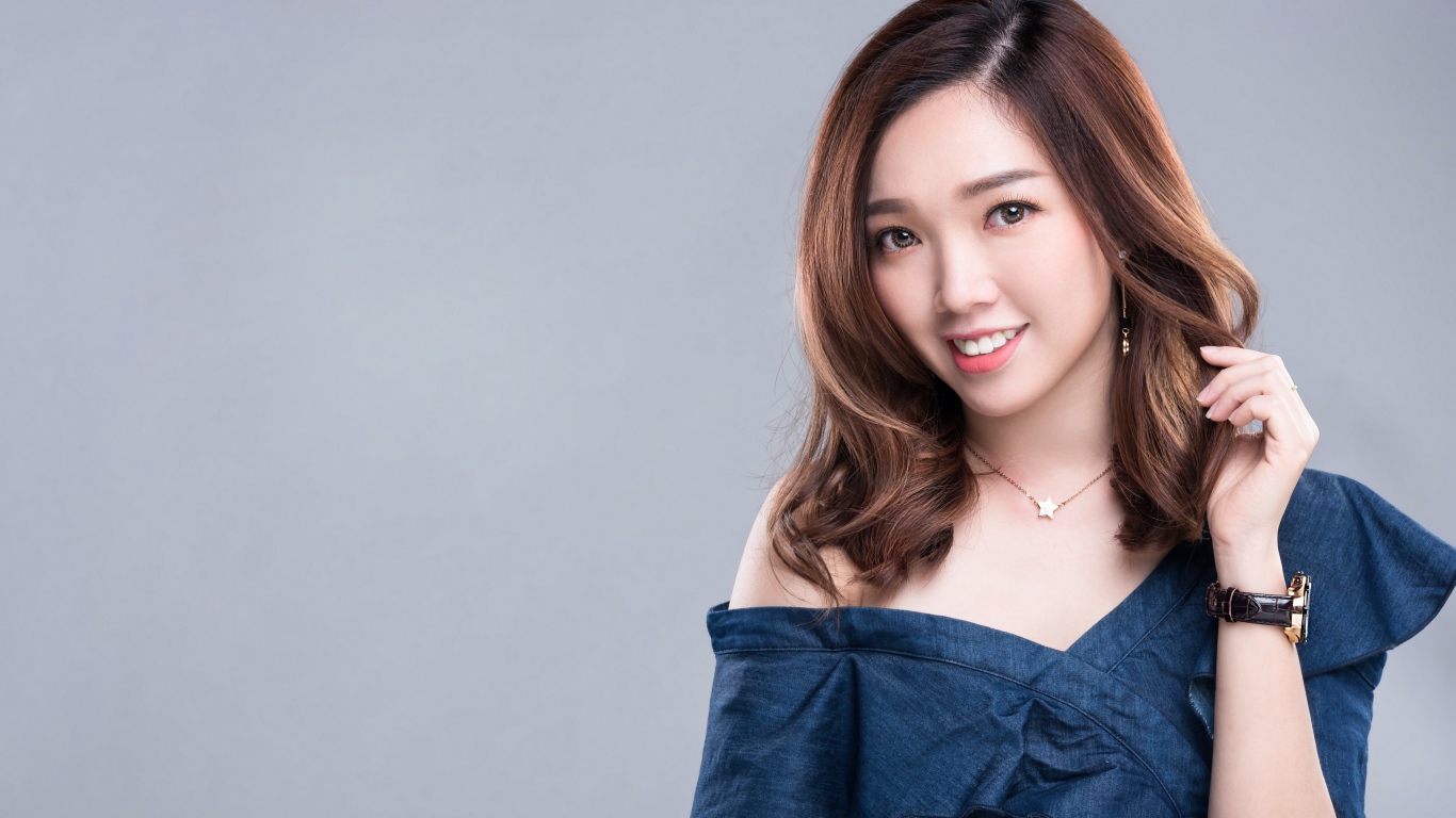 Улыбающаяся девушка азиатка с часами на руке на сером фоне