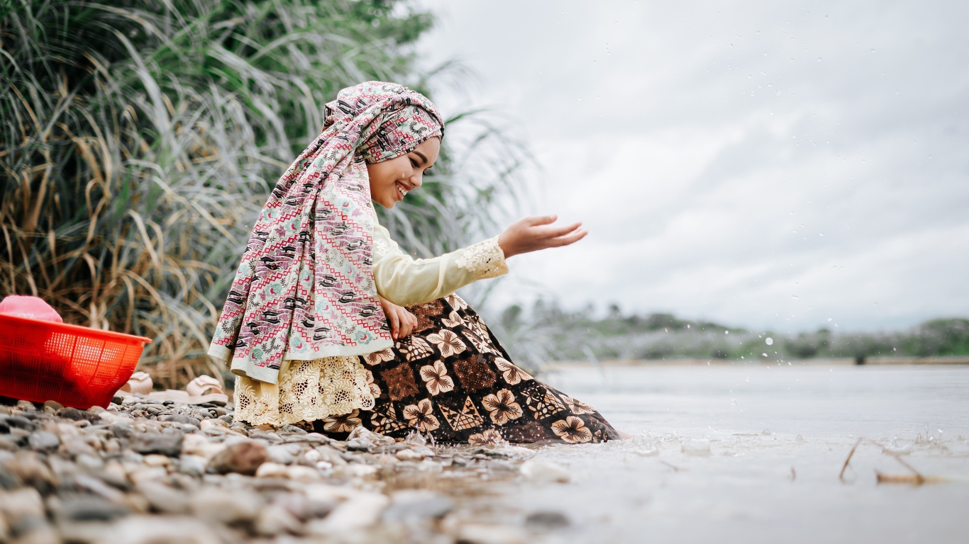 Улыбающаяся девушка азиатка сидит у воды