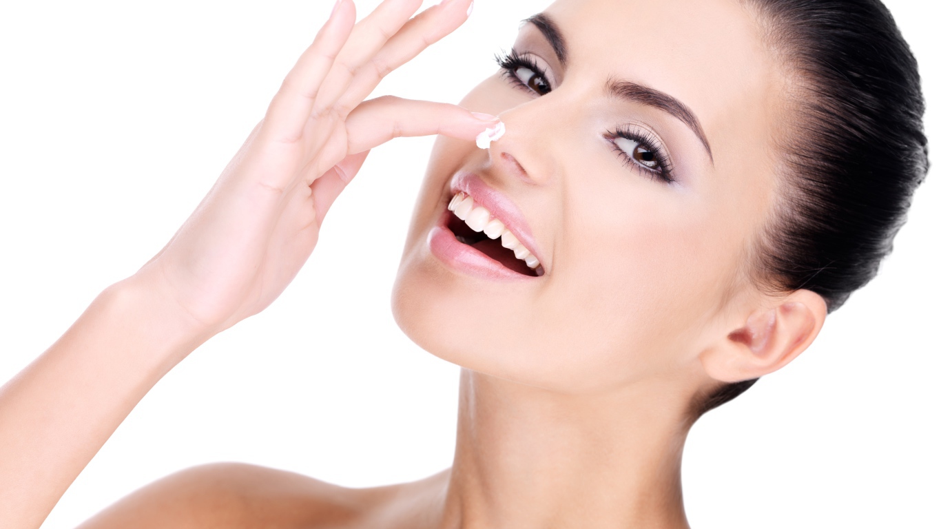 Улыбающаяся девушка мажет крем на нос 