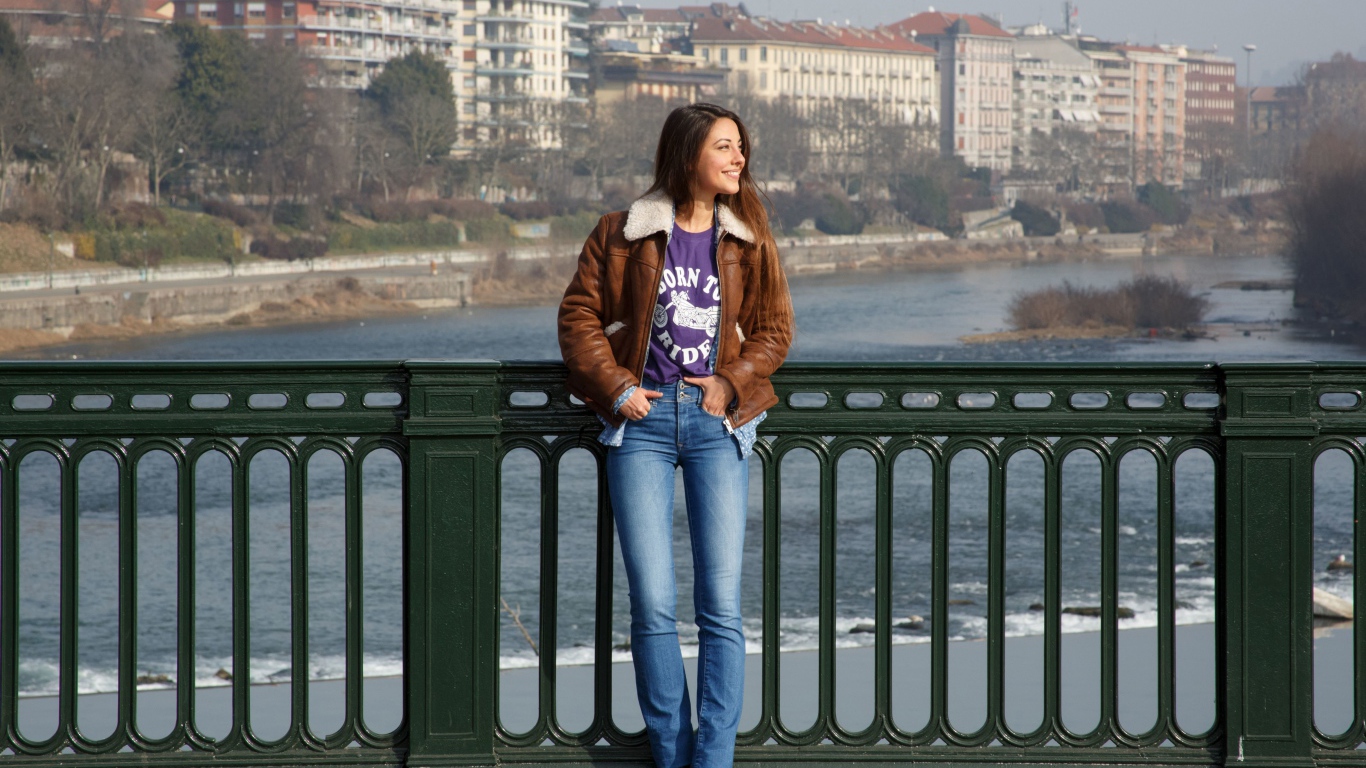 Улыбающаяся девушка стоит на мосту у реки