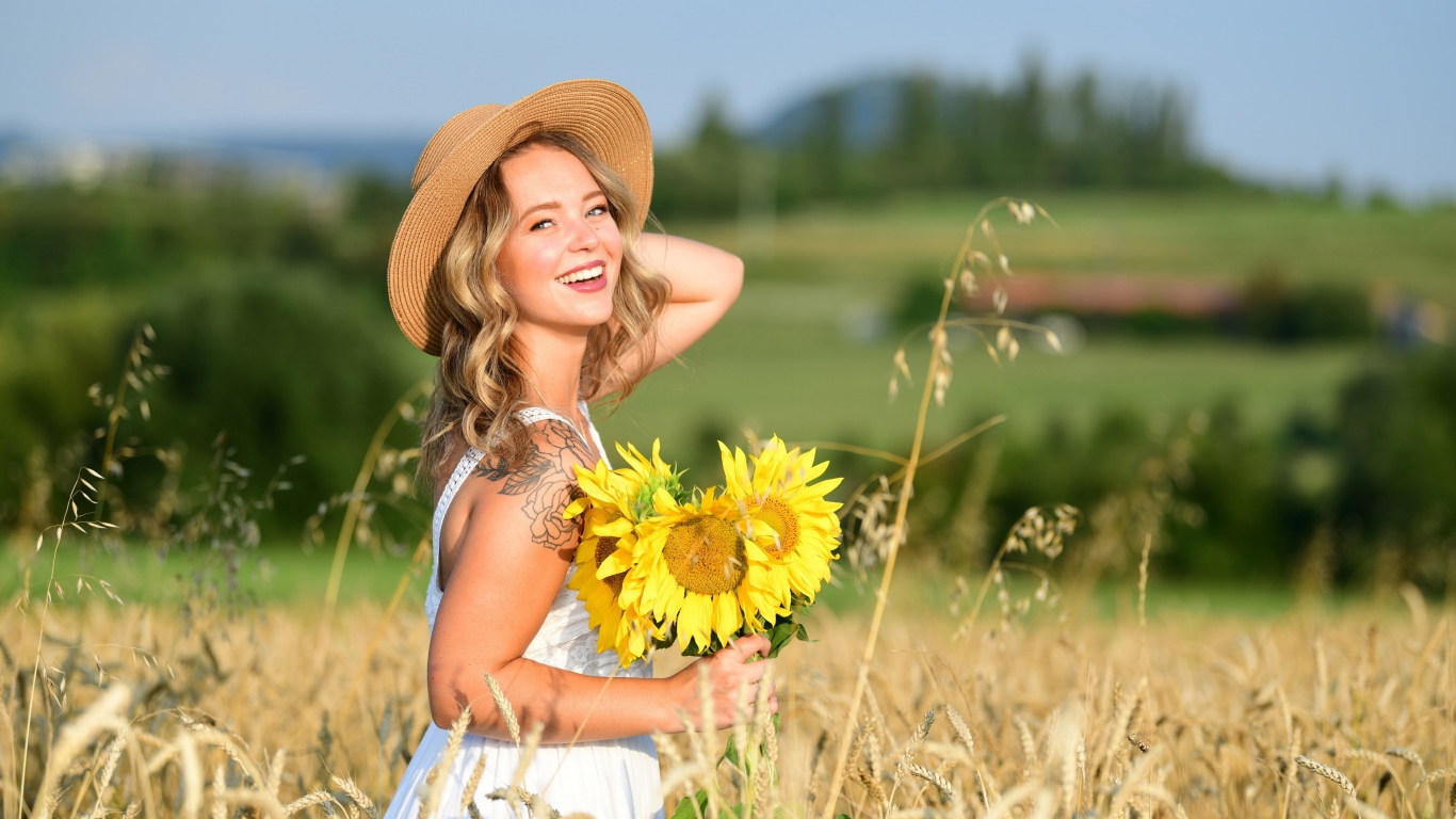 Улыбающаяся девушка с букетом подсолнухов на поле пшеницы