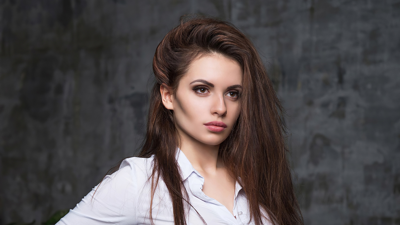 Стильная девушка в белой рубашке на фоне серой стены 