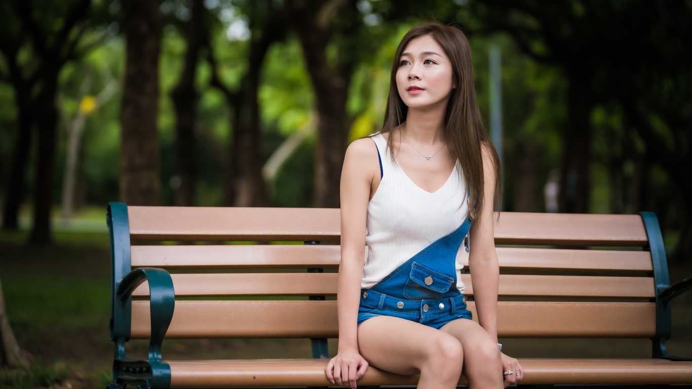 Молодая девушка азиатка сидит в парке на лавочке