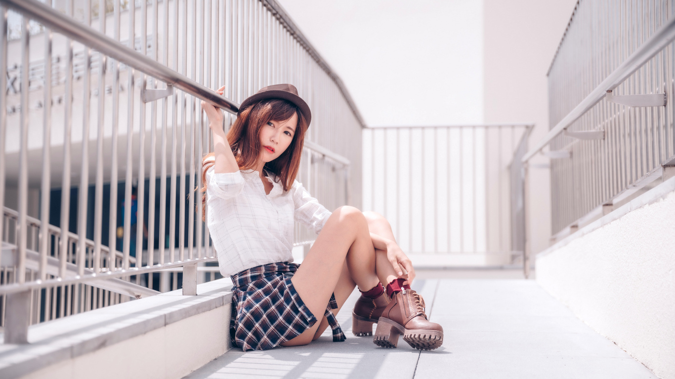 Молодая азиатка в короткой юбке сидит у перил 