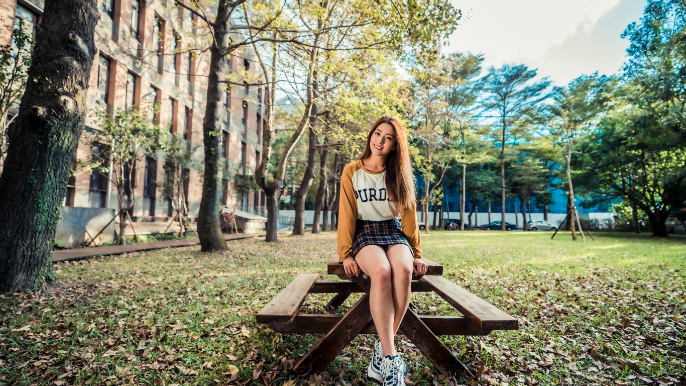 Молодая азиатка сидит на деревянном столе в парке 