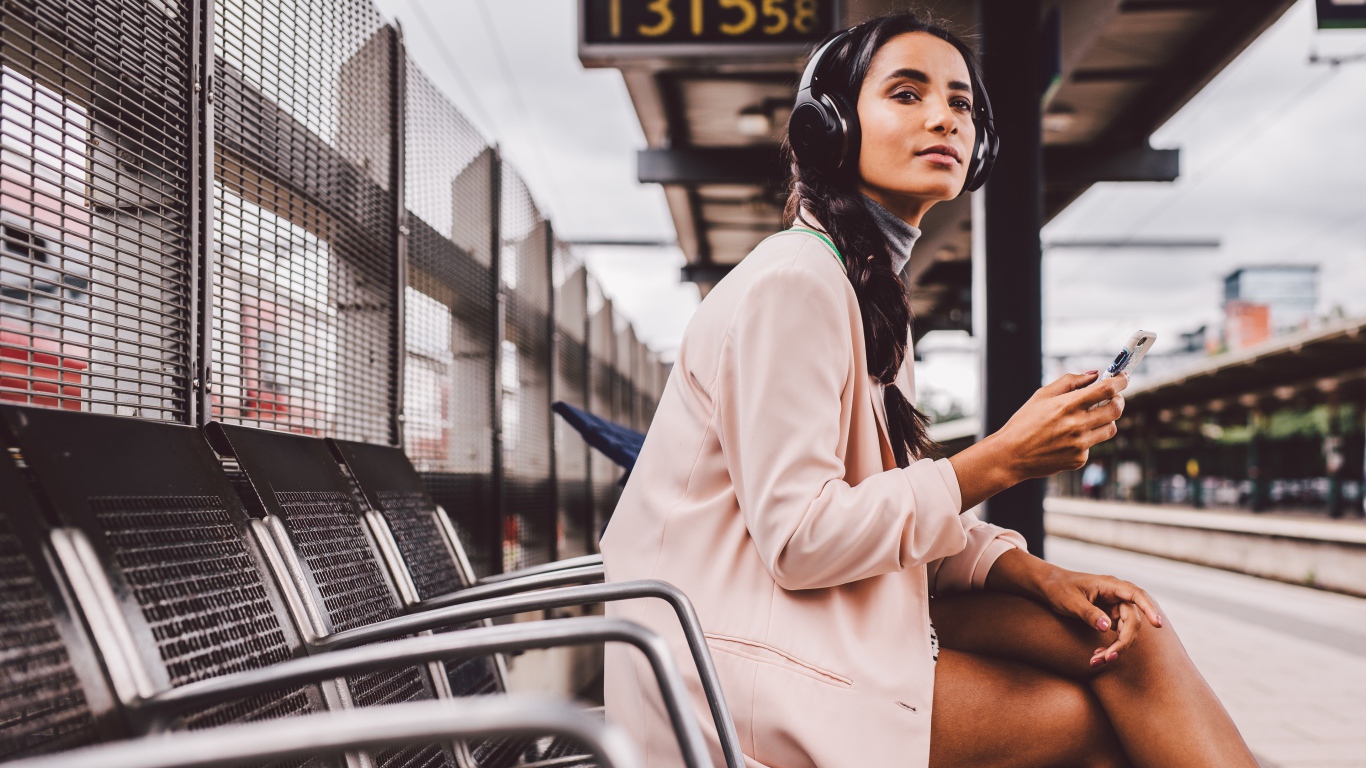 Молодая девушка в наушниках сидит на остановке