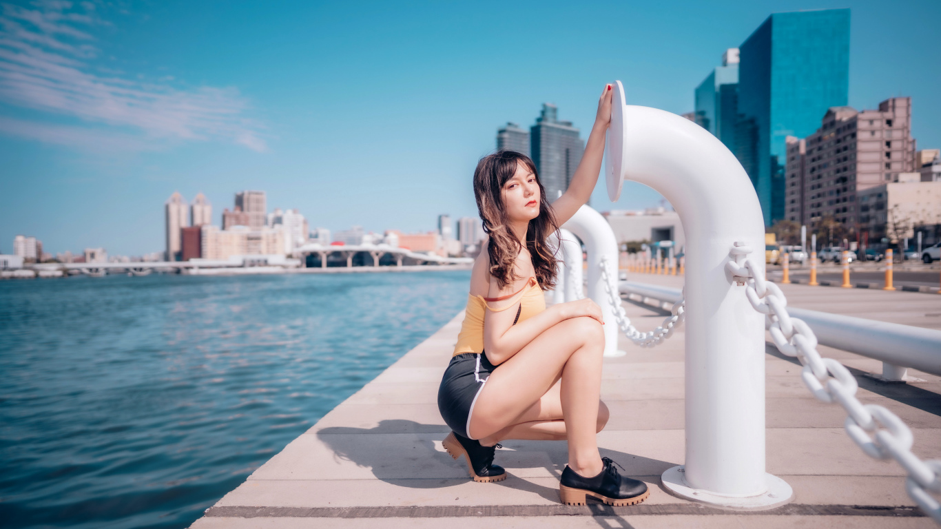 Молодая девушка в шортах сидит на пирсе