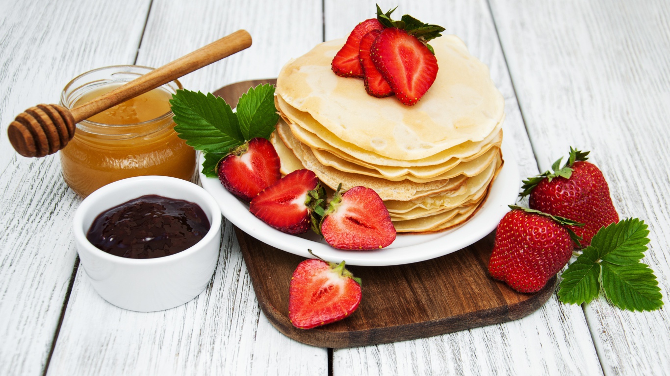 Блины с клубникой на столе с медом и джемом на праздник Масленица 2020