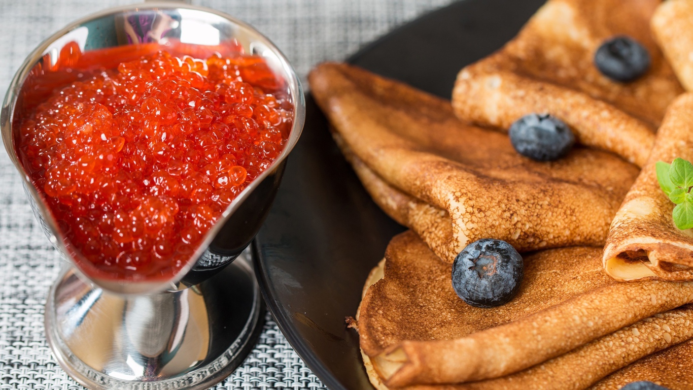 Тонкие блины с ягодами черники на столе с красной икрой на Масленицу