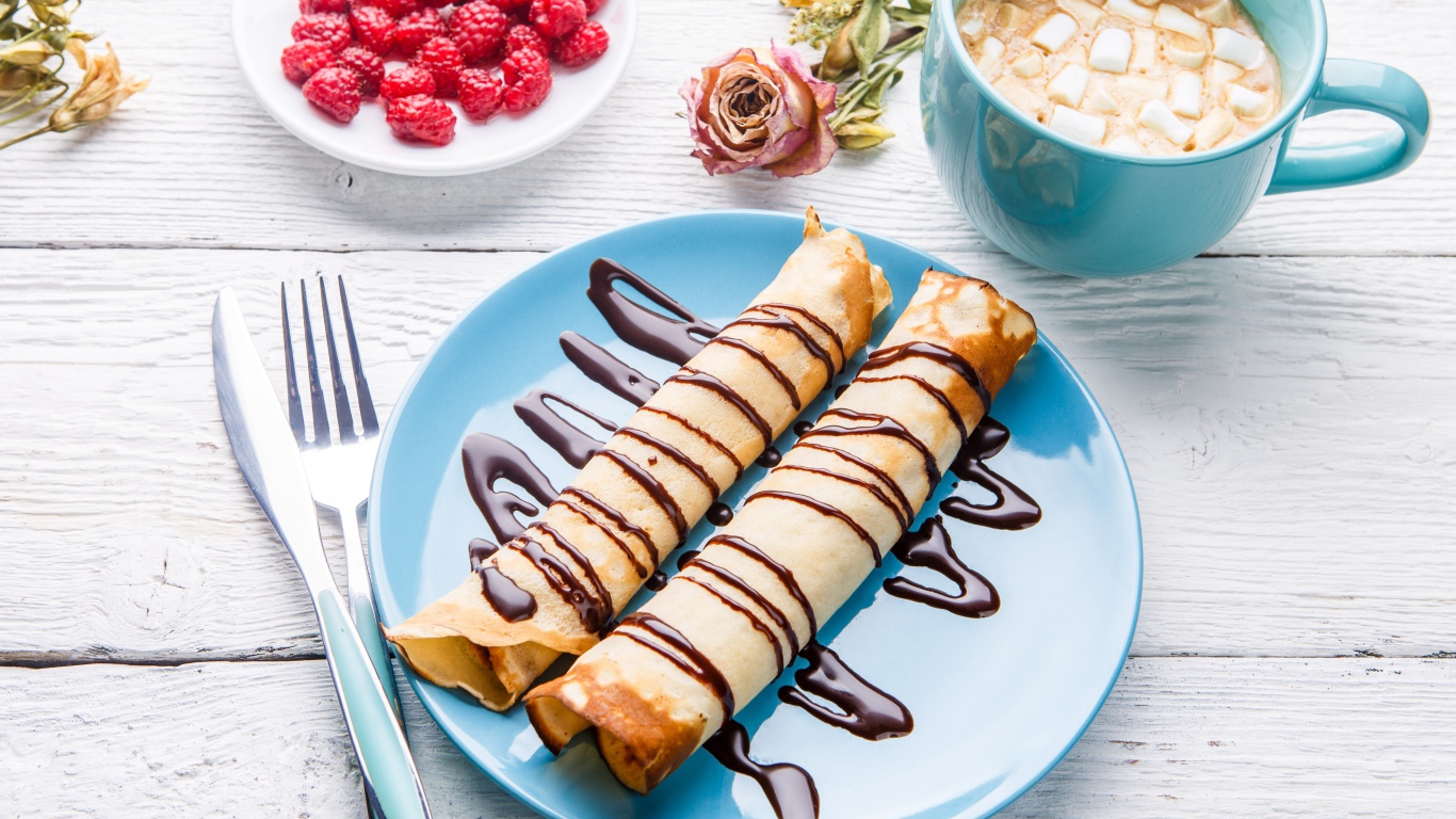 Thin pancakes with chocolate on a table with raspberries and cocoa