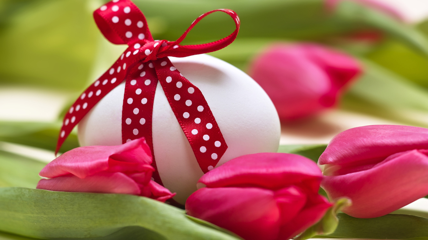 Яйцо с бантом на столе с тюльпанами на праздник Пасха