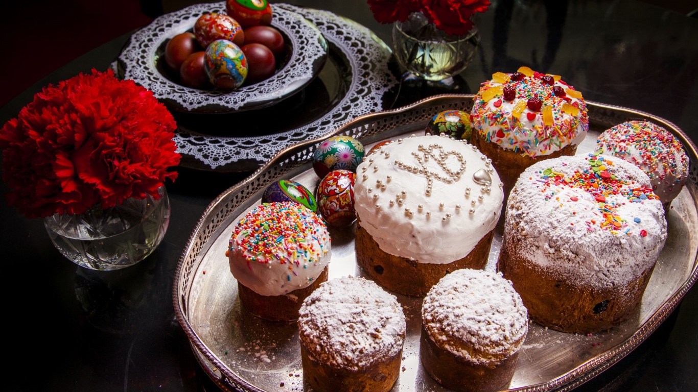 Много куличей на столе с гвоздиками и крашеными яйцами на праздник Пасха