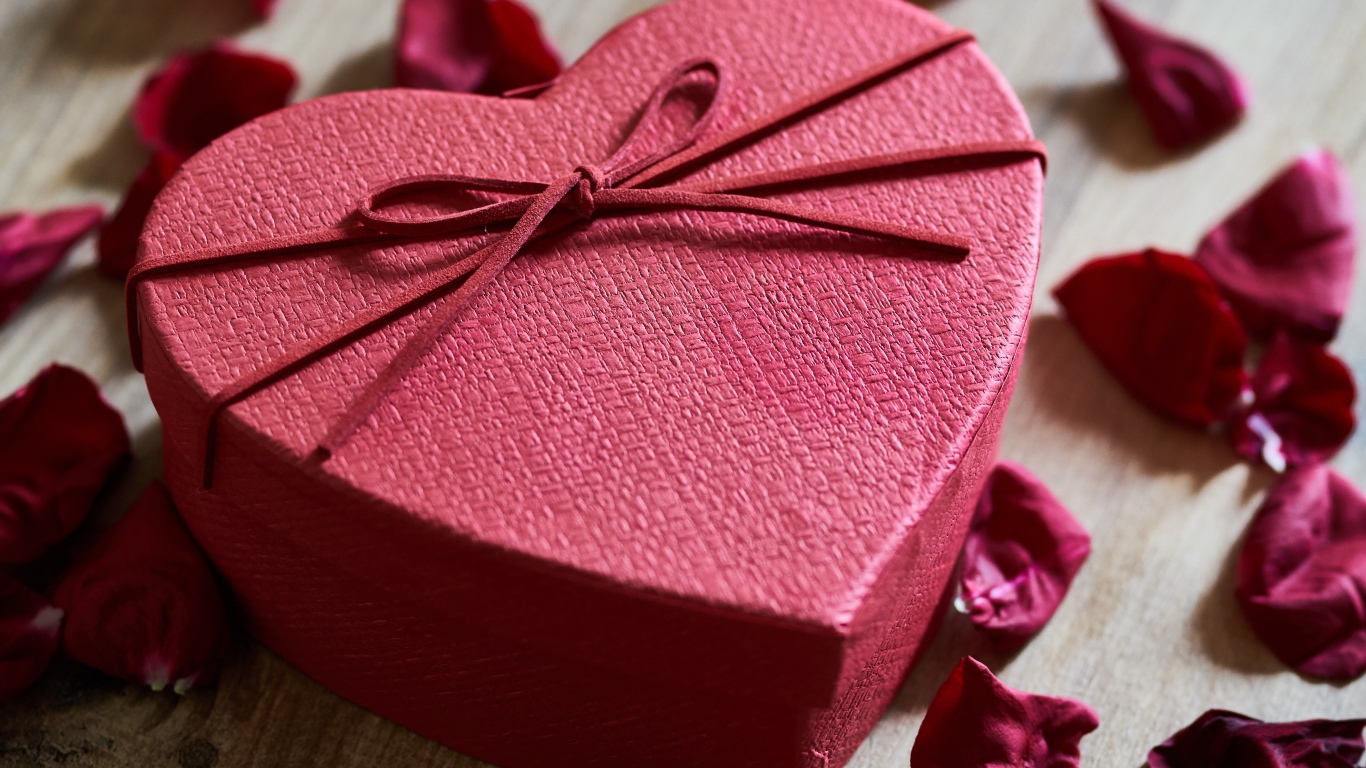 Большая красная коробка в форме сердца на столе с лепестками роз