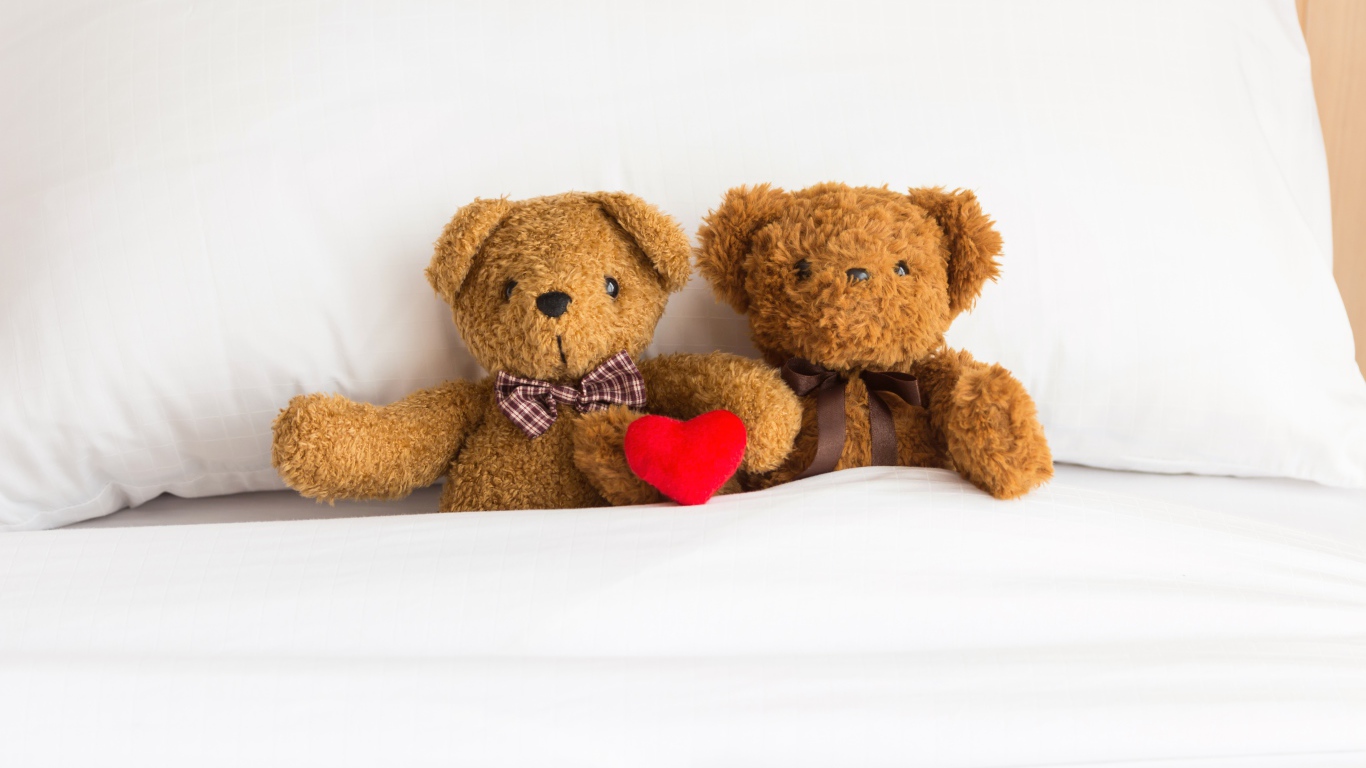 Два медвежонка Тедди лежат на кровати под одеялом 