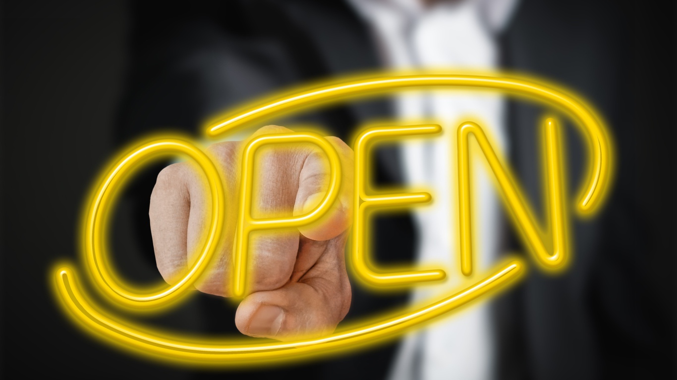 Мужчина трогает пальцем желтую  неоновую  надпись Open 