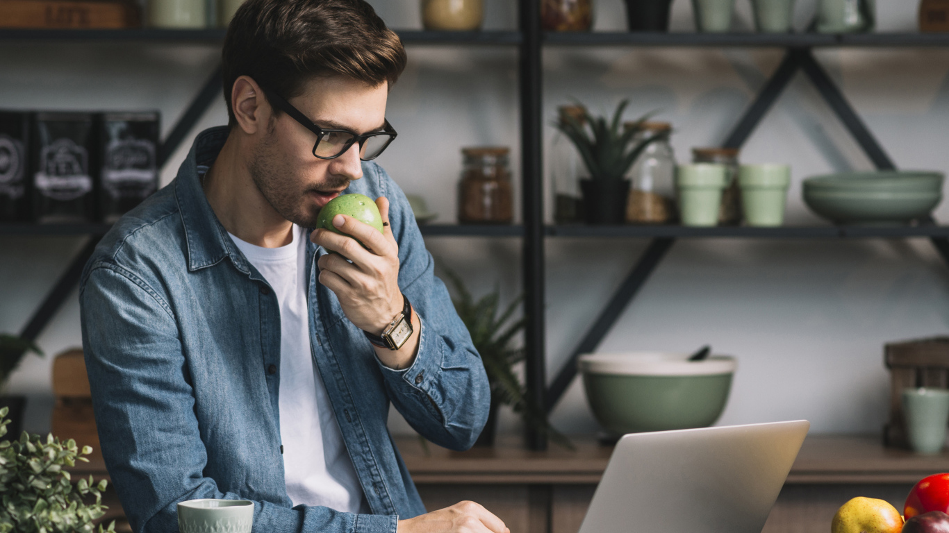Мужчина с ноутбуком ест яблоко в кафе 