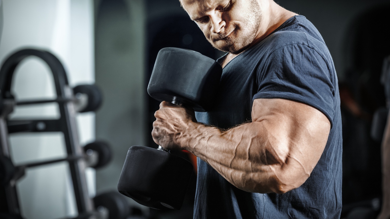 Мужчина бодибилдер в спортзале с гантелей 