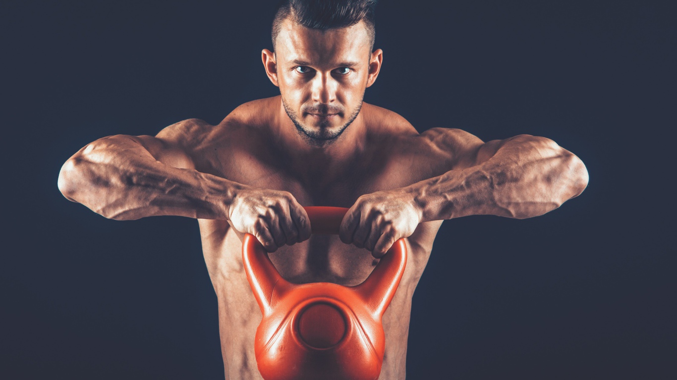 Накаченный парень поднимает тяжелую гирю на черном фоне