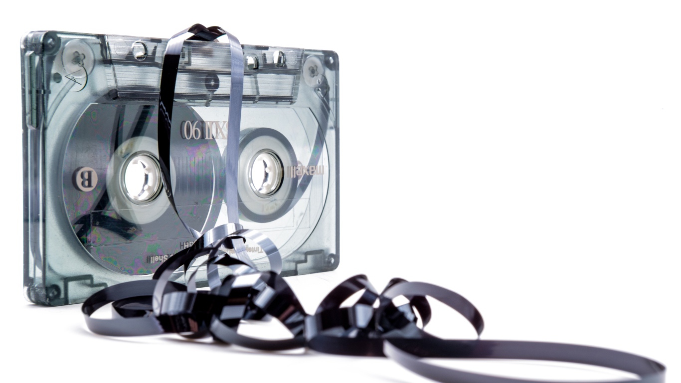 Магнитофонная кассета в размотанной пленкой на белом фоне