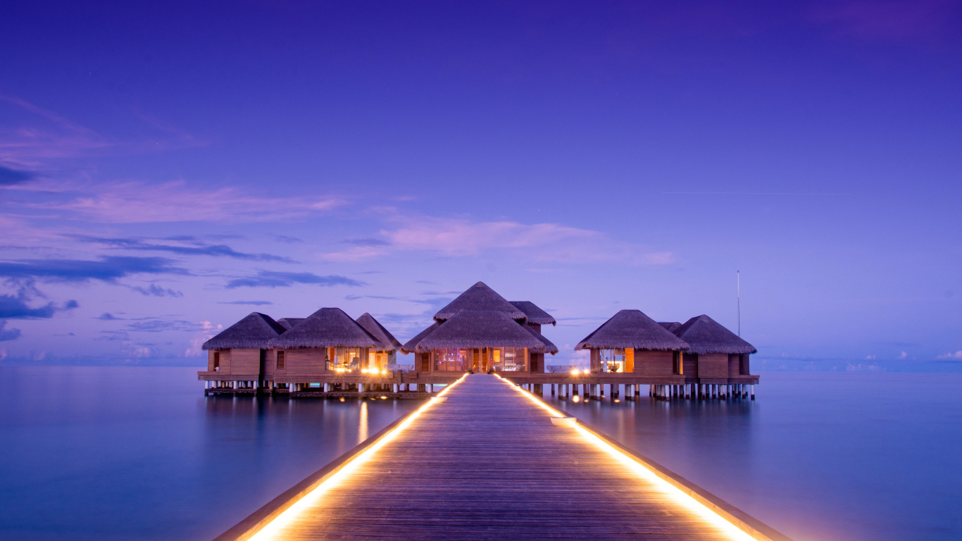 Мост с подсветкой идет к домам на сваях в океане