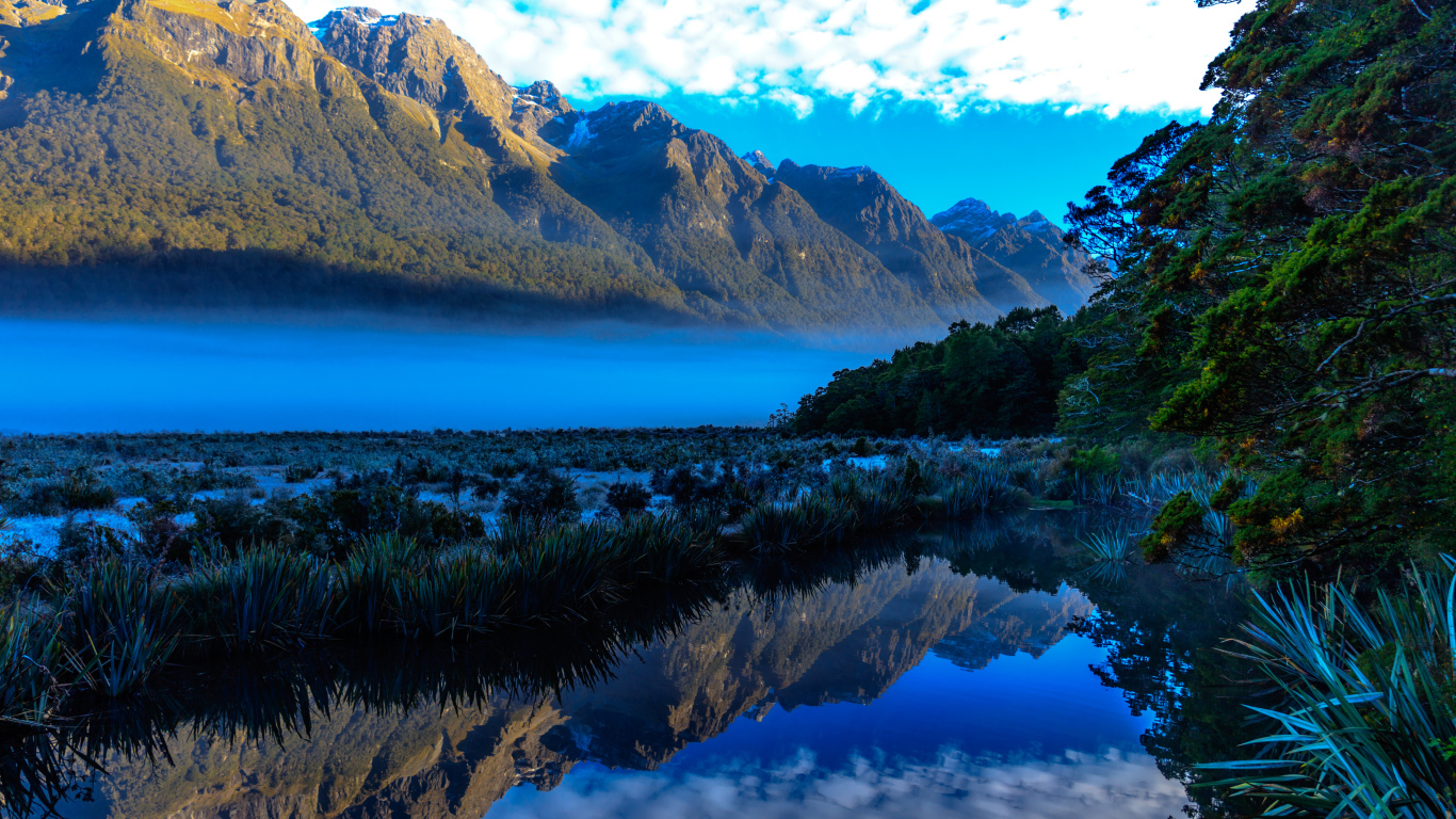 Горы и небо отражаются в голубой воде озера 