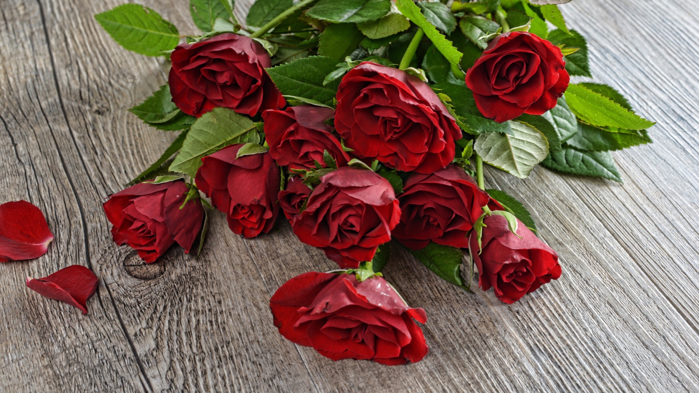 Красивый букет алых роз с зелеными листьями на деревянном столе