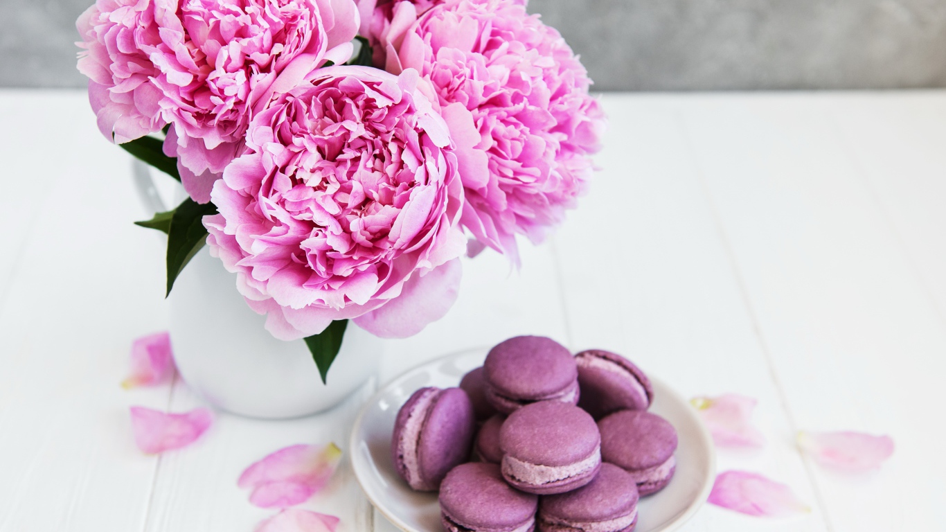 Букет розовых пионов на белом столе с десертом макарон 