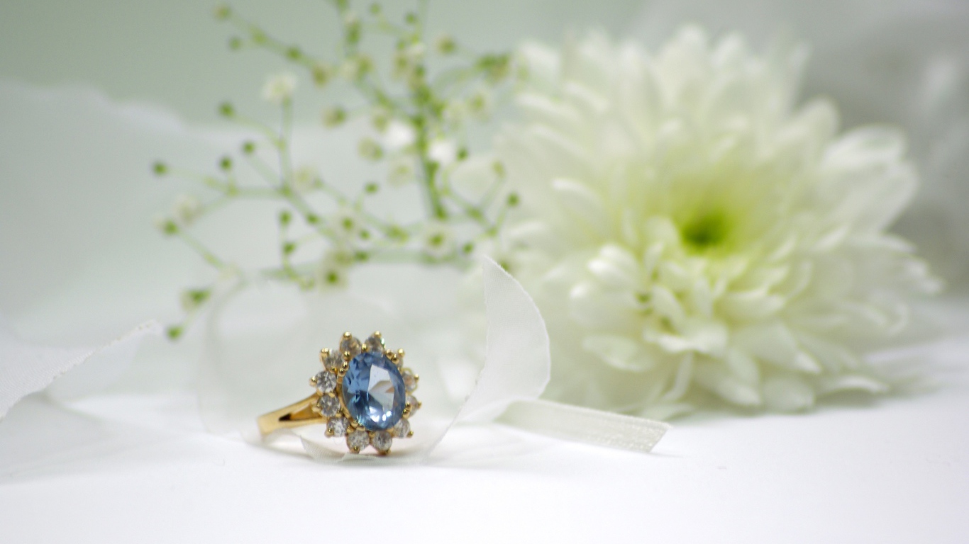 Дорогое кольцо с камнем на столе с белым цветком