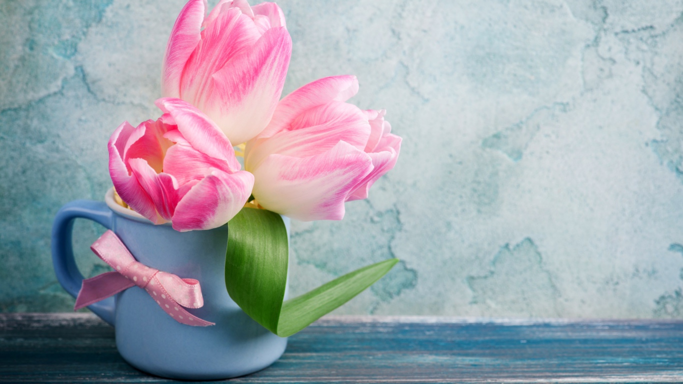 Три розовых тюльпана в чашке на столе 