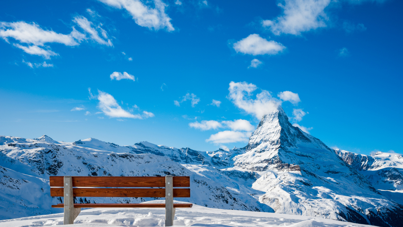 Лавка в заснеженных горах под голубым ясным небом