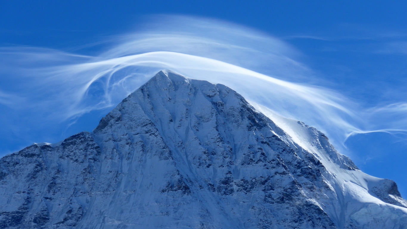 Белое облако в голубом небе над заснеженной горной вершиной